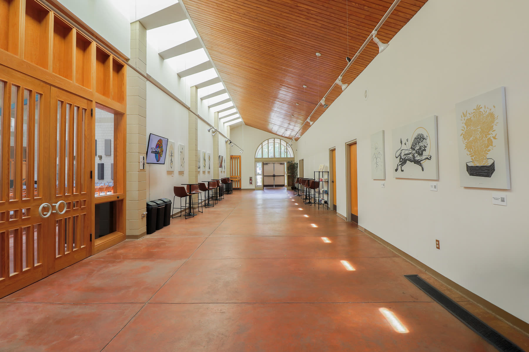 The commons: a long, light-filled hall with a wood ceiling, high windows, and café tables and stools along both walls